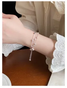 Nahaufnahme eines filigranen mehrlagigen Perlenarmbands getragen mit Spitzenmanschette