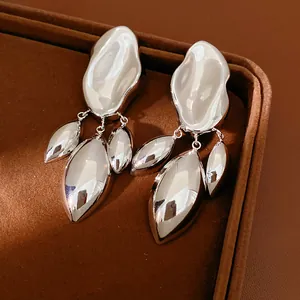 Dettaglio degli orecchini geometrici irregolari color argento su vassoio di velluto marrone.