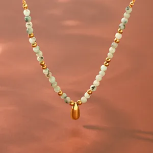 Primo piano di una collana di pietre naturali con ciondolo a goccia dorato e perline in metallo.