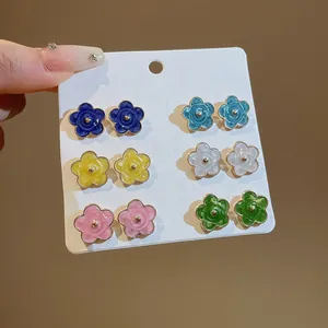 Detalle de seis pares de pendientes de botón con forma de flor de colores en tarjeta.