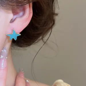 Detalle de un pendiente de estrella de mar con esmalte azul y borde dorado en una oreja