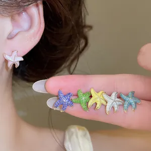 Detalle de primer plano de pendientes de estrella de mar de colores en dedo y oreja de modelo