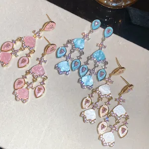 Détail de trois paires de boucles d'oreilles en zircon plaquées or 18 carats, rose, bleu, blanc.
