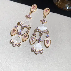 Détails de boucles d'oreilles dorées avec zircon rose et éléments en forme d'éventail blanc