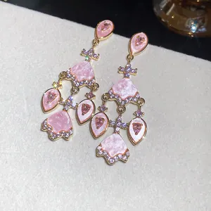 Gros plan d'élégantes boucles d'oreilles pendantes en zircon rose et détails dorés.