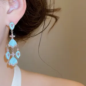 Détail de boucles d'oreilles pendantes turquoise avec pierres roses portées à l'oreille.