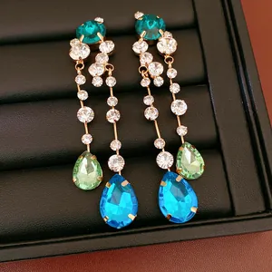 Close-up view of elegant gold-toned earrings with vibrant teardrop blue and green crystals