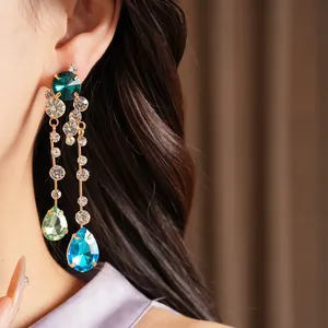 Close-up of elegant silver needle earrings with blue and green teardrop rhinestones.