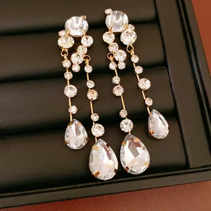 Macro detail of sparkling gold-tone long teardrop dangling earrings with round crystals