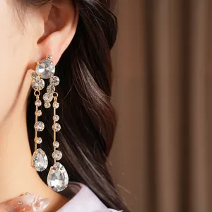 Close-up shot of elegant gold-tone rhinestone teardrop dangling earrings worn by a model