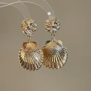 Nahaufnahme von eleganten goldfarbenen Muschel-Ohrhängern mit gehämmerten Details