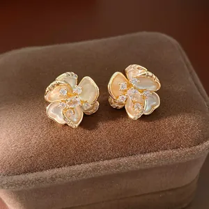Primer plano de pendientes de flores bañados en oro con circonitas brillantes y textura nácar