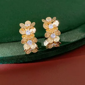 Close-up of gold C-shaped earrings with wrinkled flowers and sparkling zircon inlay