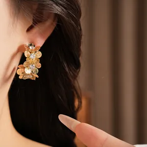 Close-up of golden pleated flower C-shaped stud earrings with zircon stones on a model ear.
