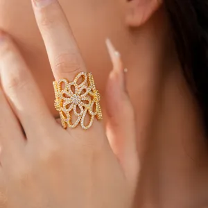Detailed close-up of an 18K gold plated hollow flower ring with zircons worn on a finger