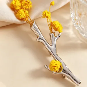 Detailaufnahme einer silbernen Ast-Brosche, die elegant gelbe Trockenblumen hält
