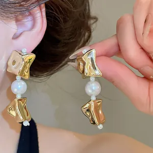Detailed view of irregular gold metal earrings with white pearl accents on model