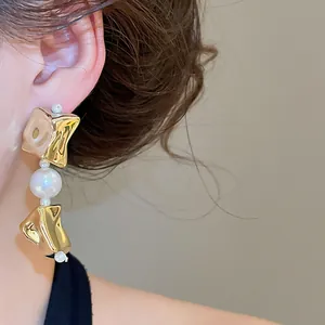 Detailed macro view of irregular gold-tone earrings with elegant white pearls on a model
