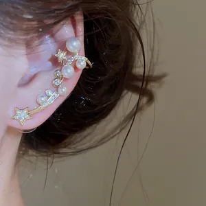 Détail d'une boucle d'oreille earcuff dorée avec perles et zircons en forme d'étoile.