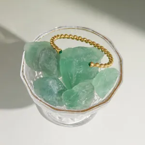 Close-up of a gold twisted cuff bracelet featuring green gemstones inside a glass bowl