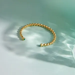Detailed view of the twisted gold stainless steel cuff bracelet with green gemstones.