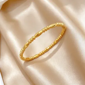 Close-up of a minimalist gold titanium steel bangle with zen staff pattern on satin