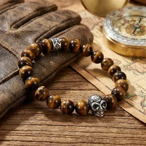 Close-up of tiger eye stone beads with vintage skull and cross charms on leather background