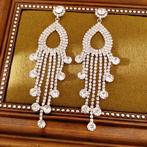 Orecchini a nappa in argento con strass scintillanti posati su sfondo verde oliva