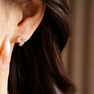 Close-up detail of sparkling zircon hollow clover ear hoops worn on a model's ear.