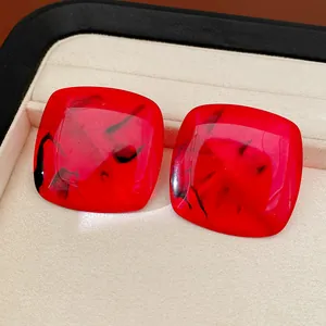 Close-up of square red resin stud earrings with black marbled texture in a jewelry box