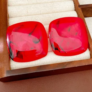 Detailed close-up view of red resin square stud earrings with unique black marbled patterns
