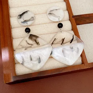 Close-up detail of silver needle resin earrings with ink-wash patterns on a jewelry tray