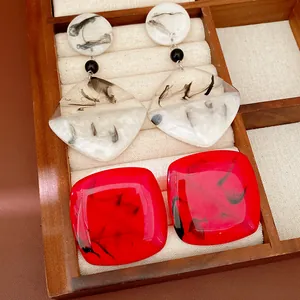 Close-up detail of red and white resin earrings with ink-wash patterns in a wooden tray