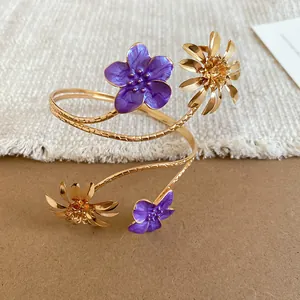 Eleganter goldfarbener Oberarmreif mit lila Emaille-Blumen und Metall-Gänseblümchen.