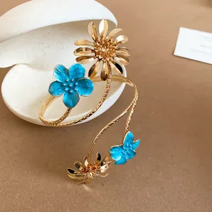 Nahaufnahme goldener Spiral-Armreif mit leuchtend blauen Emaille-Blumen und Metallblättern
