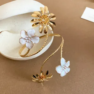 Detailaufnahme eines goldenen Blumen-Oberarmreifs mit weißen Emaille-Blüten und Metallband