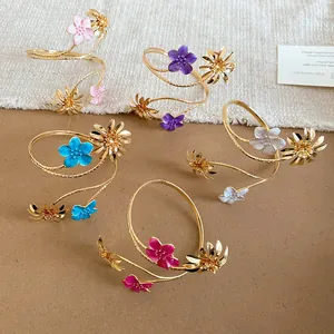 Bunte Armbänder mit Emaille-Blumen und goldenen Gänseblümchen-Details auf Stoffhintergrund