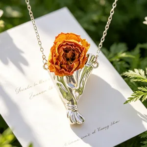 Macro di una collana d'argento con una vera rosa essiccata arancione in un ciondolo a bouquet