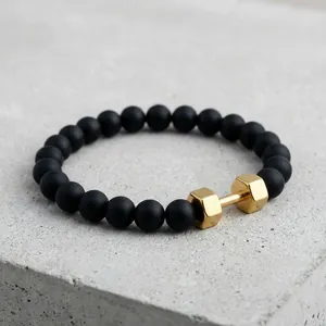 Men's matte black agate beaded bracelet with a golden dumbbell charm on stone background