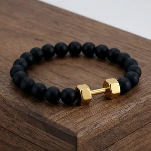 Macro detail of matte black onyx beads with a polished gold dumbbell charm on a bracelet