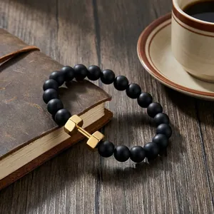 Close-up of black onyx beaded bracelet with a gold barbell charm on a leather notebook
