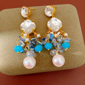 Macro detail of elegant gold geometric dangle earrings with faceted glass crystals and pearls
