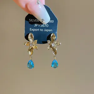 Detailed view of gold flower stud earrings featuring elegant blue teardrop stones