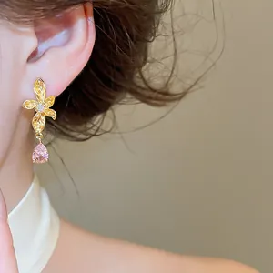 Detailed close-up view of elegant golden flower stud earrings with a pink teardrop zircon