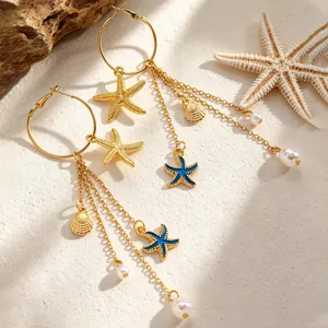 Détail de boucles d'oreilles pendantes étoile de mer et coquillage sur fond de sable.