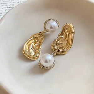 Detailed macro view of gold ear-shaped earrings with faux pearl and crystal accents