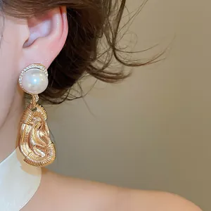 Detailed view of exaggerated ear-shaped gold drop earrings with a large pearl accent.
