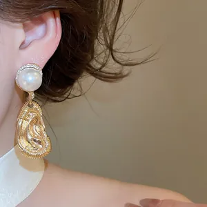Close-up of exaggerated ear-shaped pearl drop earrings with an elegant golden finish