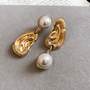 Macro detail of unique gold ear-shaped earrings featuring elegant white pearl drops.