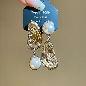 Detail view of unique mismatched gold ear-shaped earrings with pearl drops on a display card.